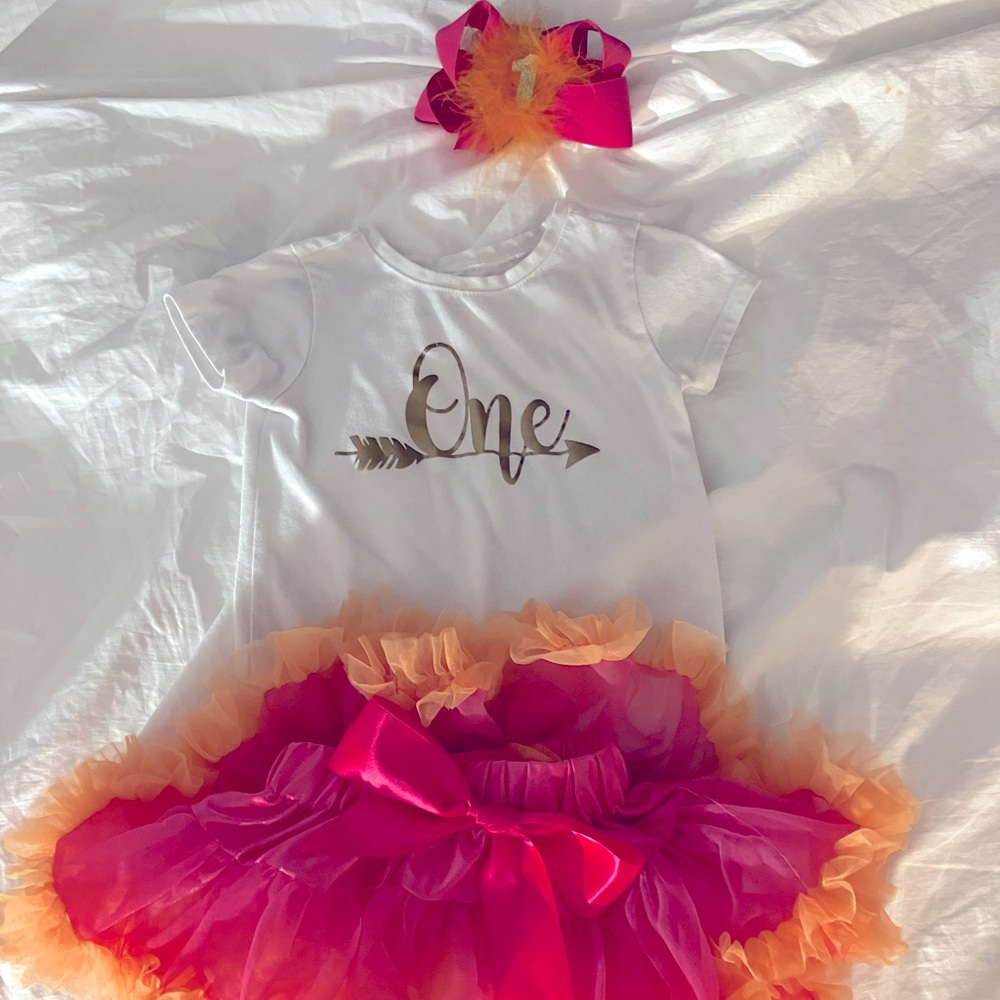 Orange/hot pink tutu with matching”1” bow. Gold “one” on white tshirt.